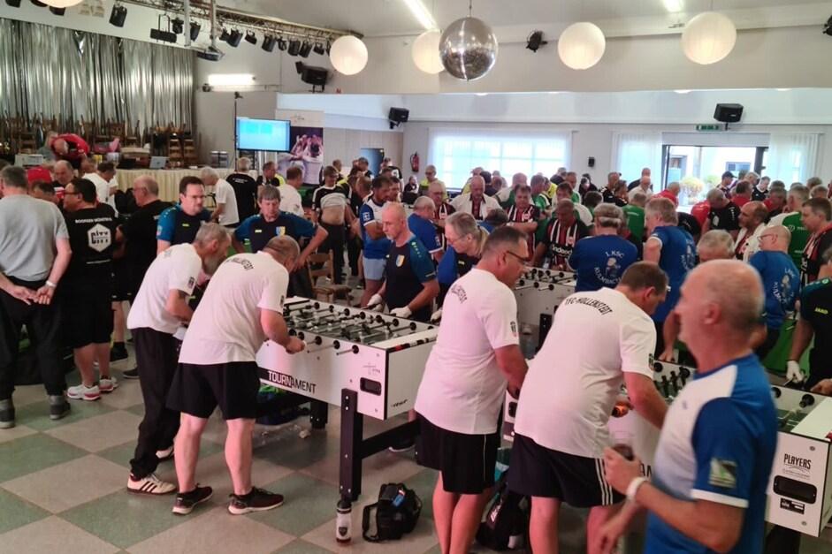 Volles Turnier mit zahlreichen Teilnehmern, die an mehreren Tischkickern in einem großen Saal spielen.